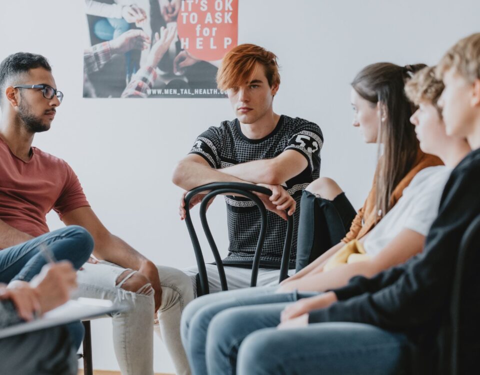 A group of teenagers sit in a circle during a group therapy session.