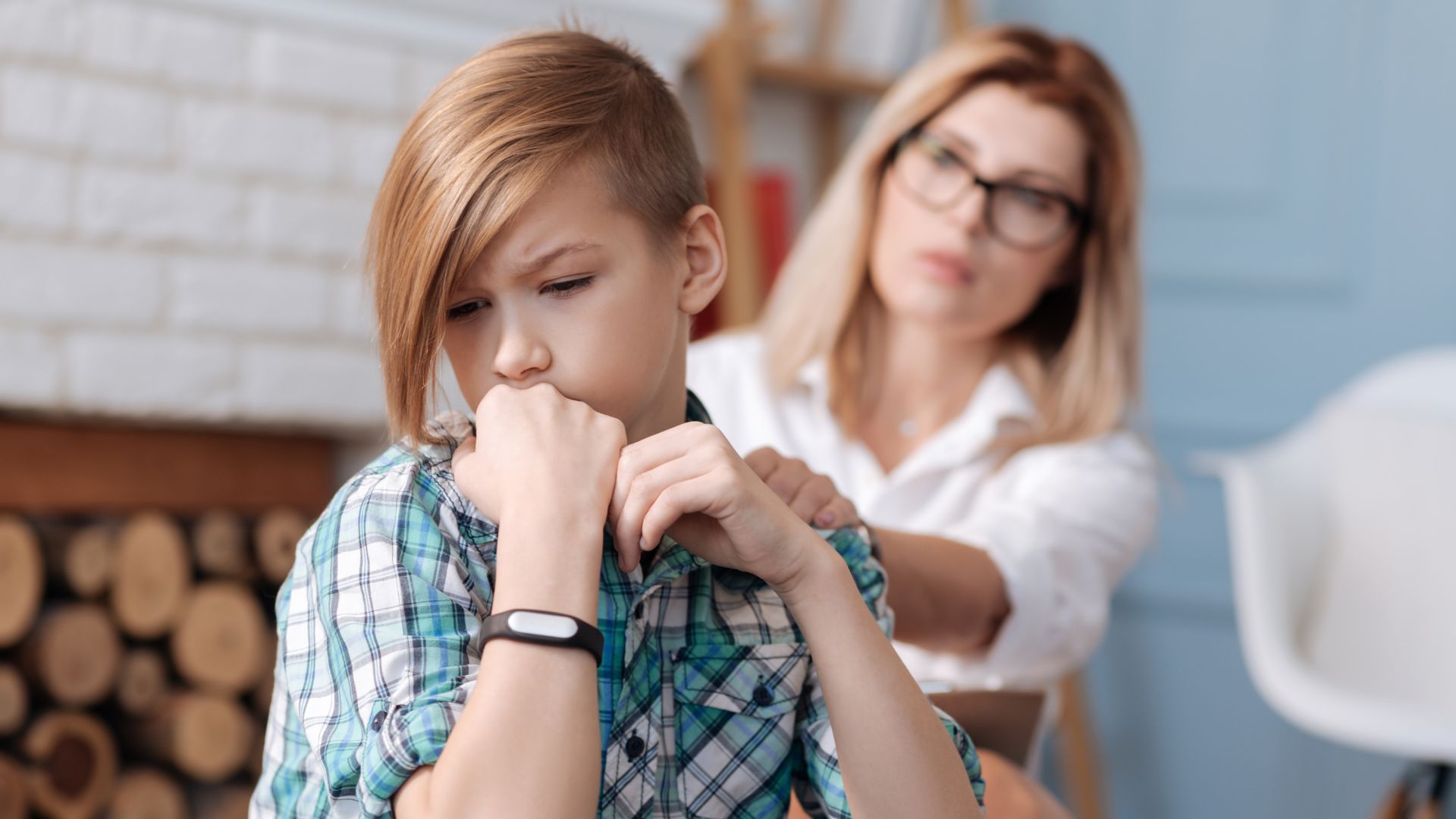 A mother wearing glasses reaches out and touches the shoulder of her son, who looks sad.