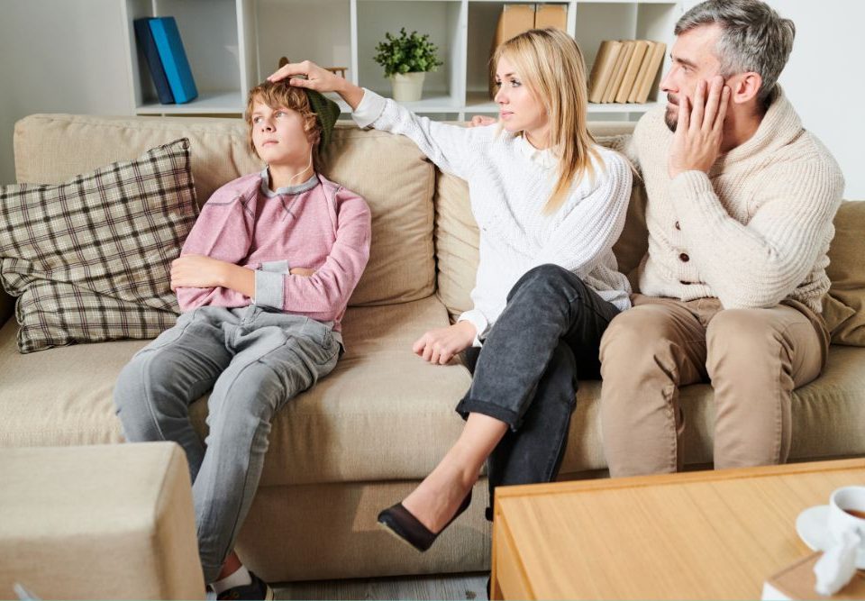 A mother and father consider therapy for their teenage son as they sit on the couch near him.