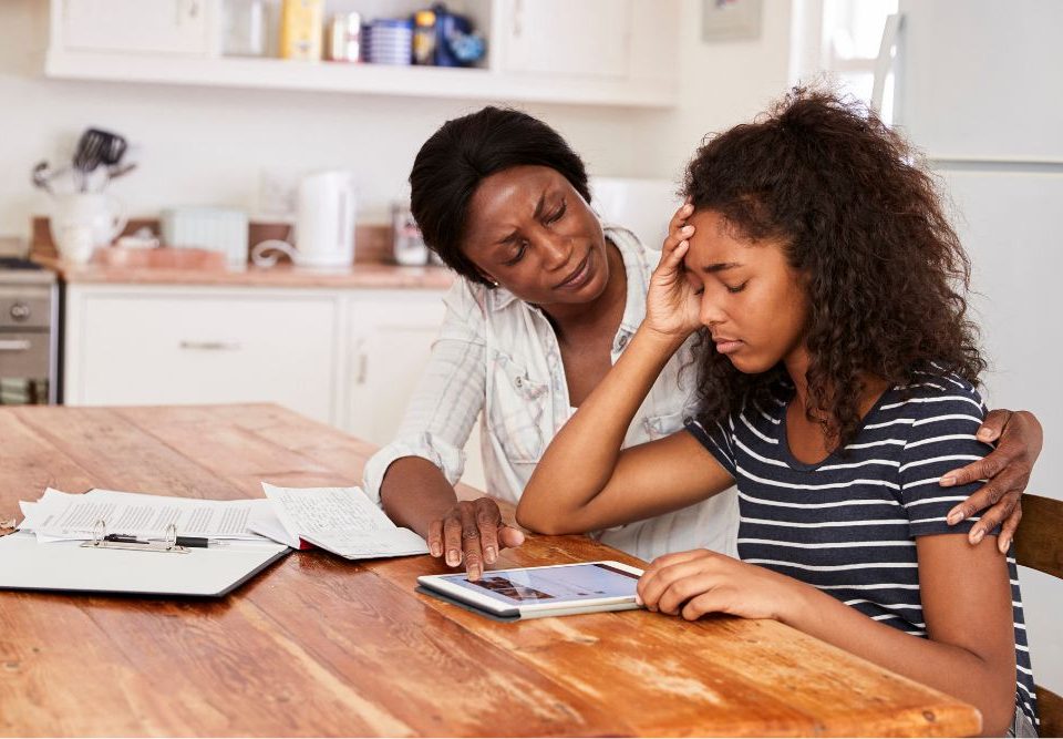 Teen depression impacts more than 3% of adolescents each year. In this picture a mother puts her arm around her teenage daughter as they sit at a kitchen table.