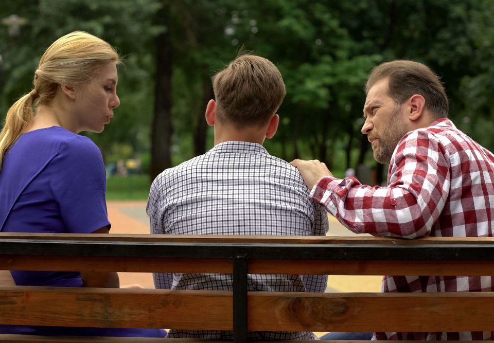When should parents consider more intensive treatment for a child with mental health issues? In this photo a mom and dad sit on other side of a teenage boy on a park bench. They are having a serious conversation about mental health.
