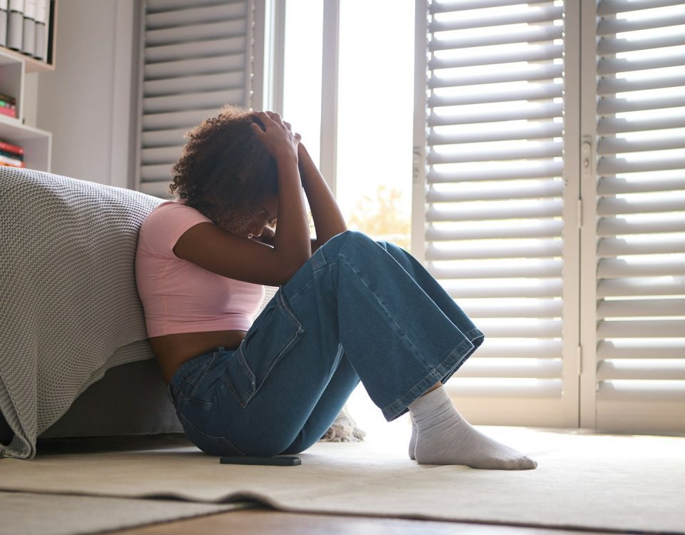 Anxious Teenage Girl Sitting On Bedroom Floor At Home With Mobile Phone Concerned About Social Media