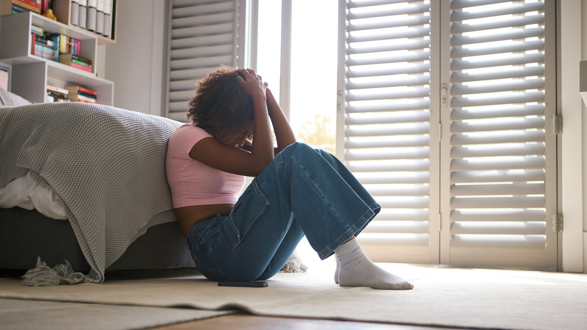 Anxious Teenage Girl Sitting On Bedroom Floor At Home With Mobile Phone Concerned About Social Media