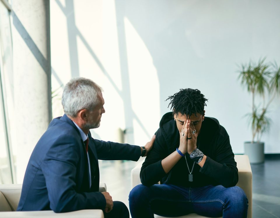 Depressed African American teenager having a meeting with his therapist at psychotherapy center.