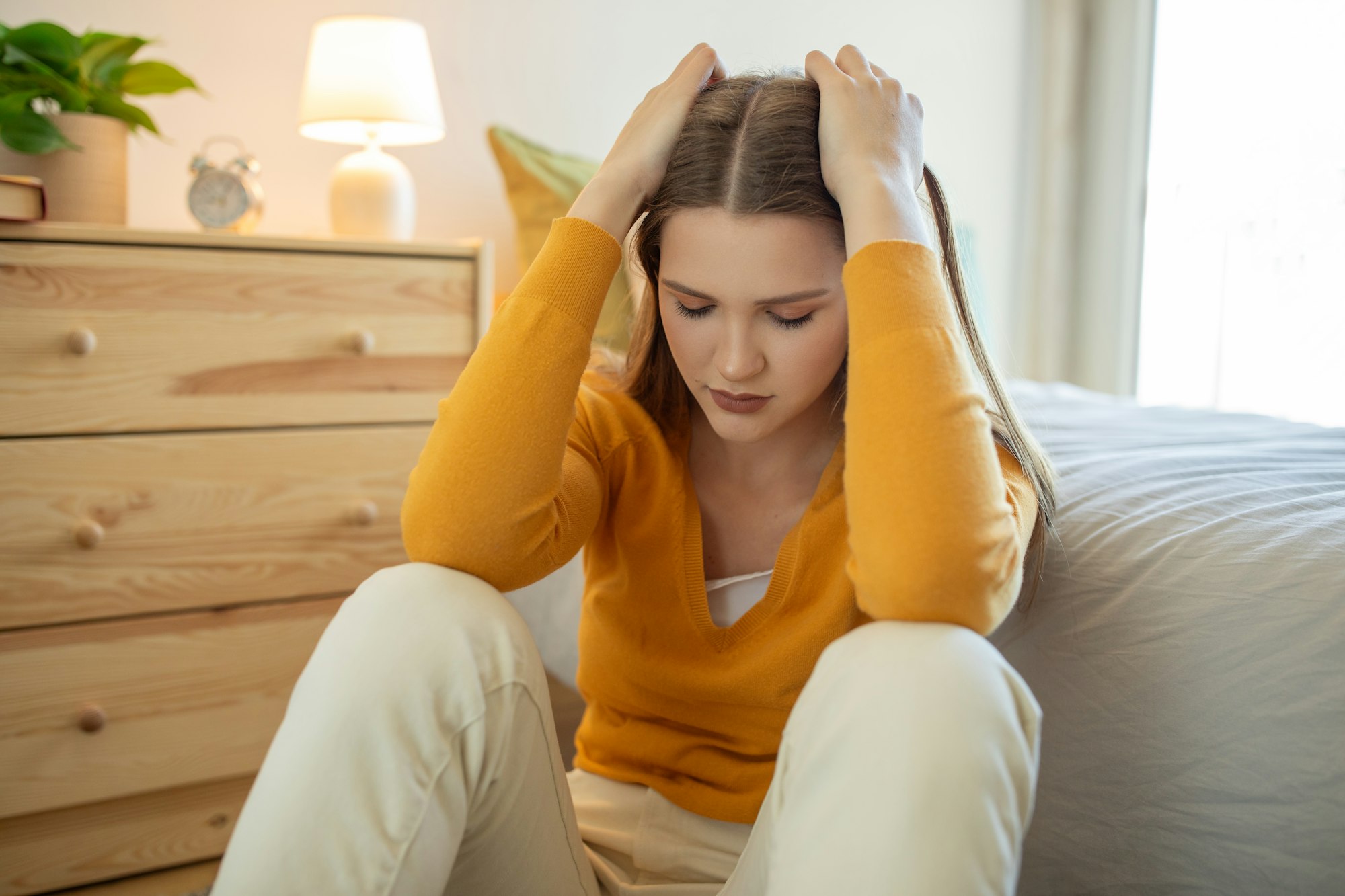 Teen Girl Sitting on Bedroom Floor Appearing Upset in Daylight