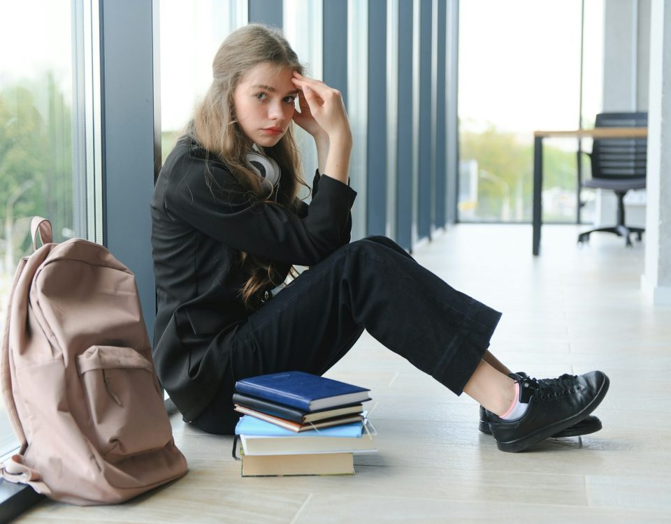 Upset teen girl sit on floor sadly look out window worried about teenage problem at school