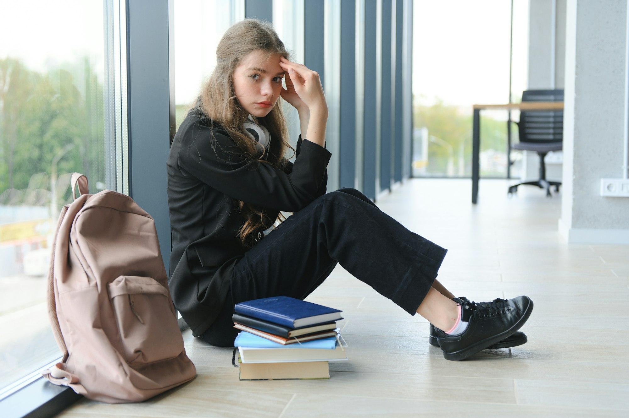 Upset teen girl sit on floor sadly look out window worried about teenage problem at school