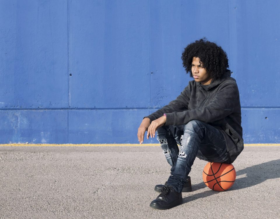 african american teen sitting on basketball ball