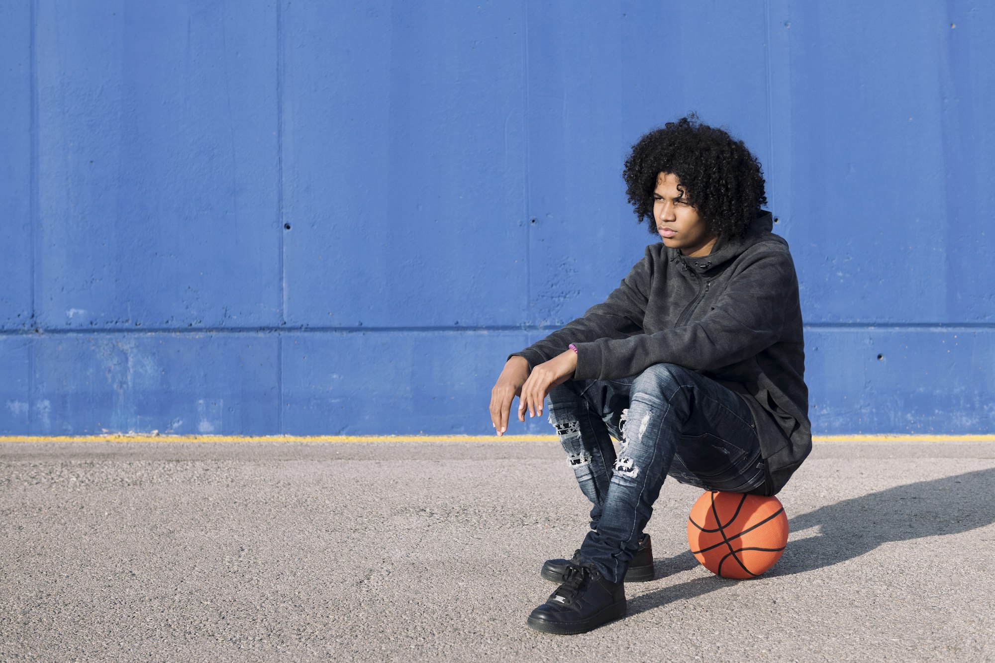 african american teen sitting on basketball ball