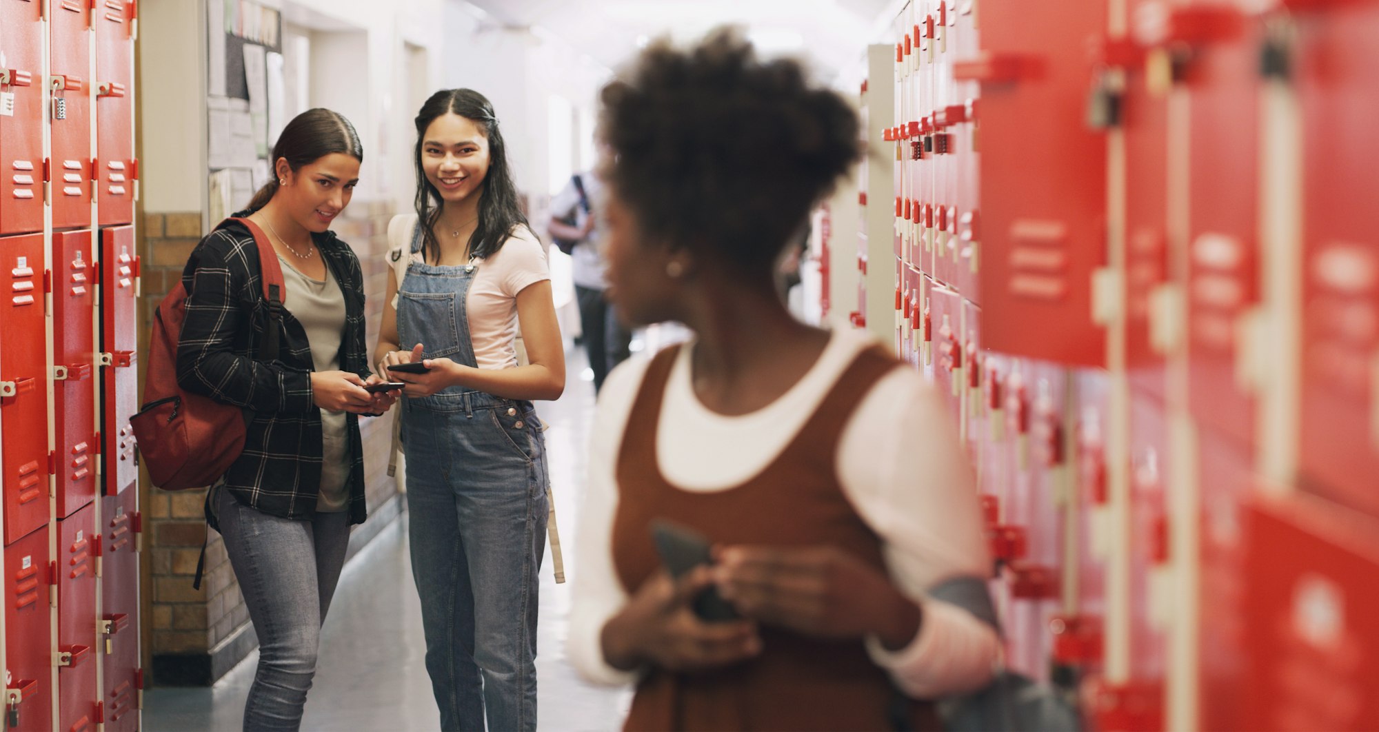 Shot of a teenage girl using a smartphone next to her locker and being bullied at high school