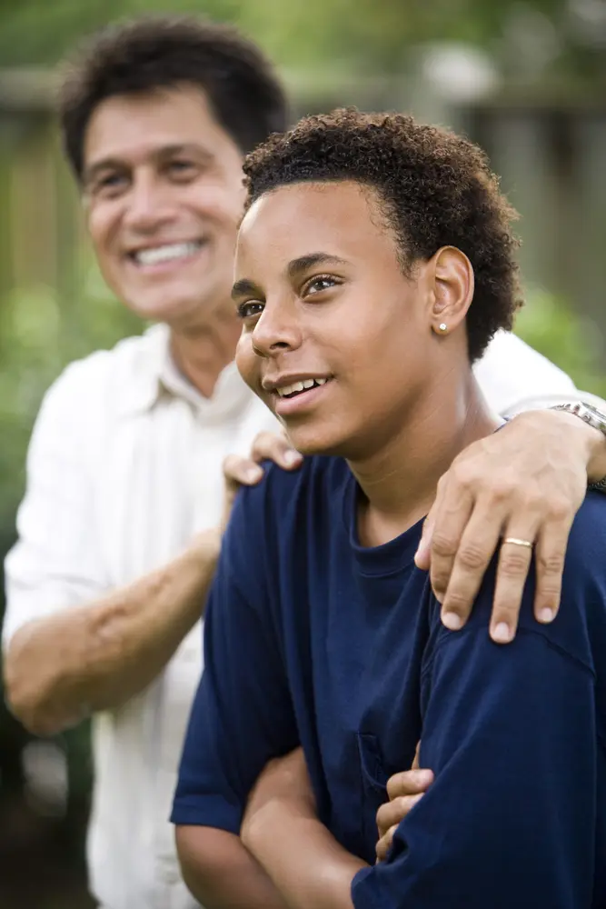 Male teen smiling and sitting beside smiling male adult.