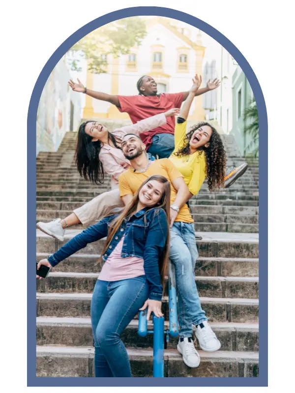 Five smiling teens posing energetically on stairs with their hands and arms in the air.