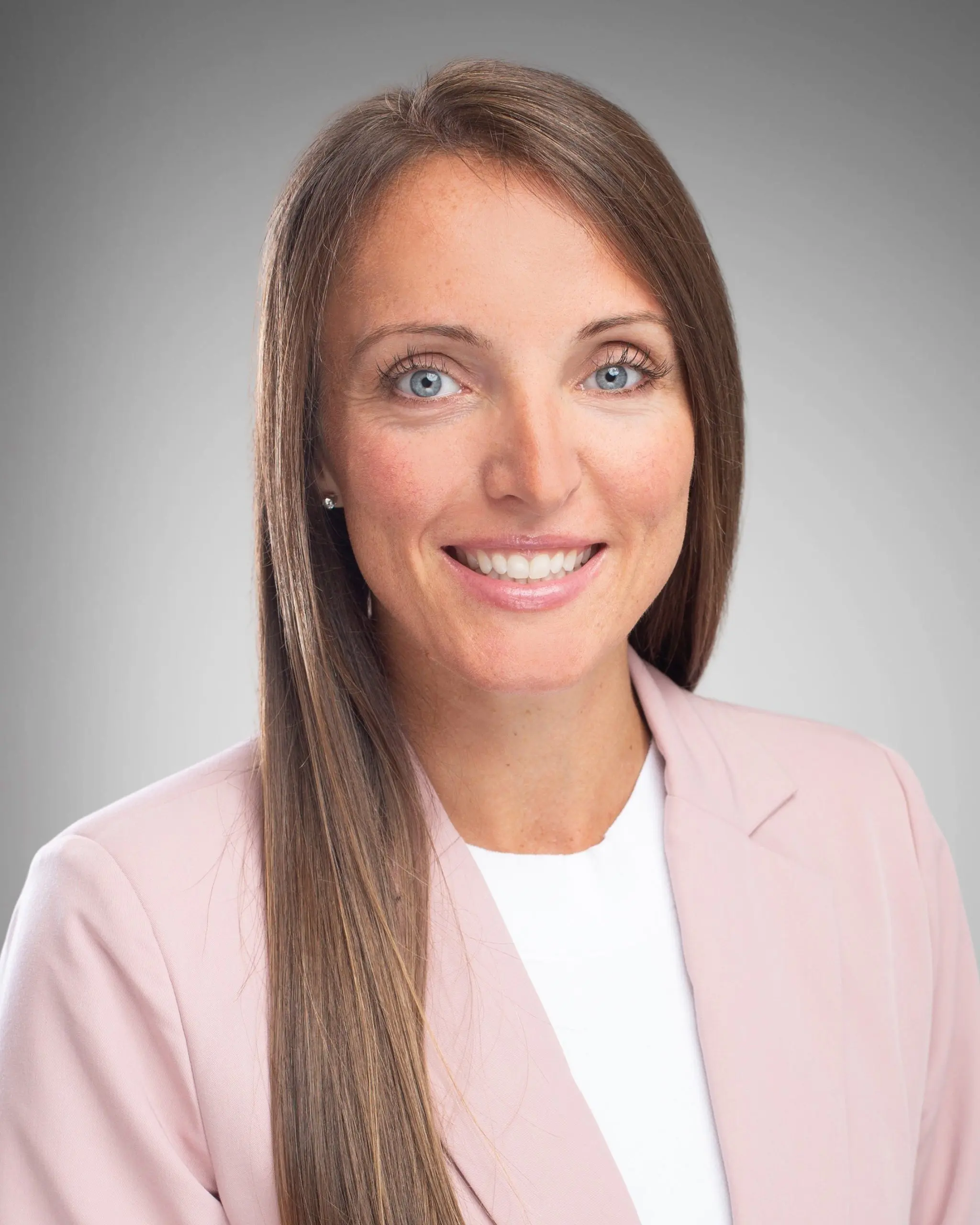 Woman in a light suit smiling with brown hair.