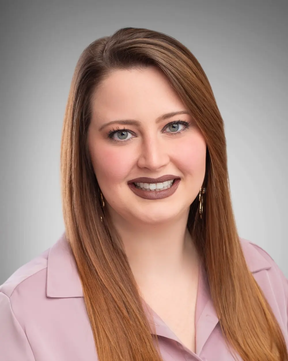 Smiling woman wearing a pink shirt with brown hair.