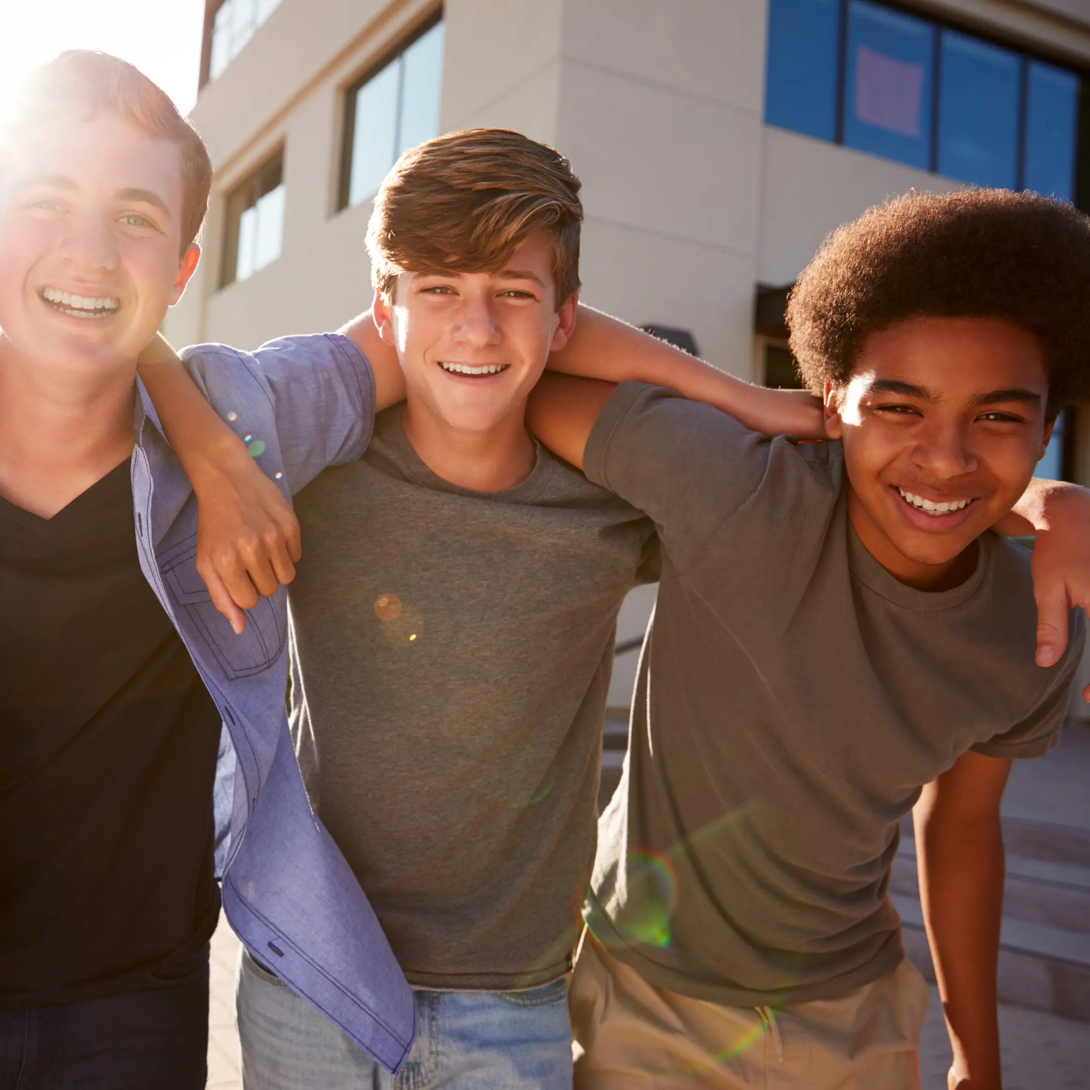 Three young men smiling with their arms on each others shoulders.