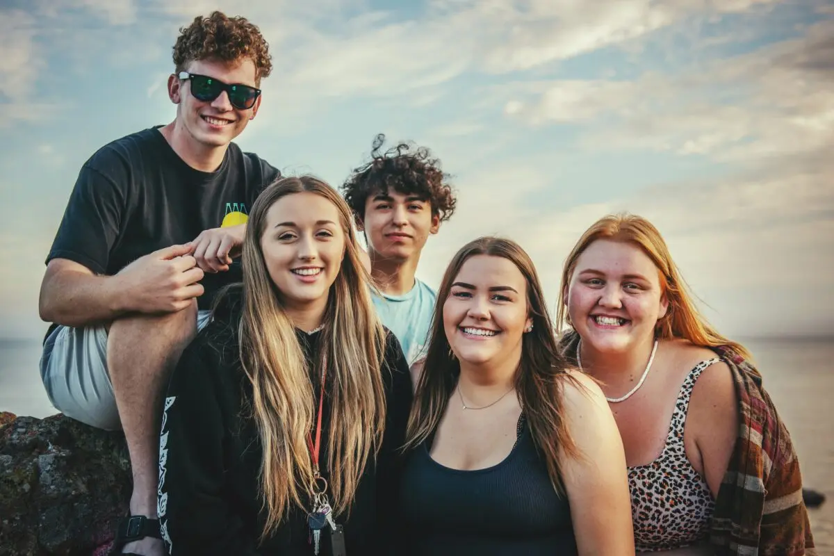 Five teens in an outdoor setting, standing together for a photo, smiling.