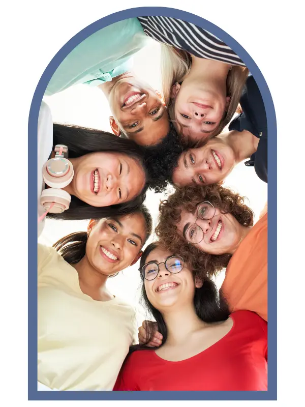 Seven teens leaning towards each other with their heads touching as they look down and smile.