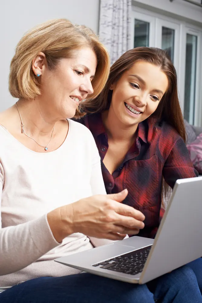 Mother at daughter at a laptop smiling.