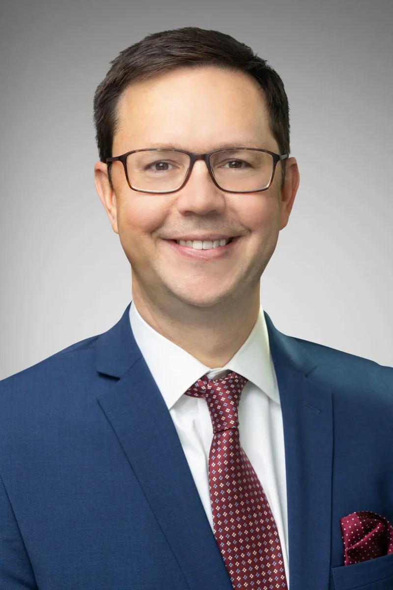 Man in a navy suit smiling with brown hair.