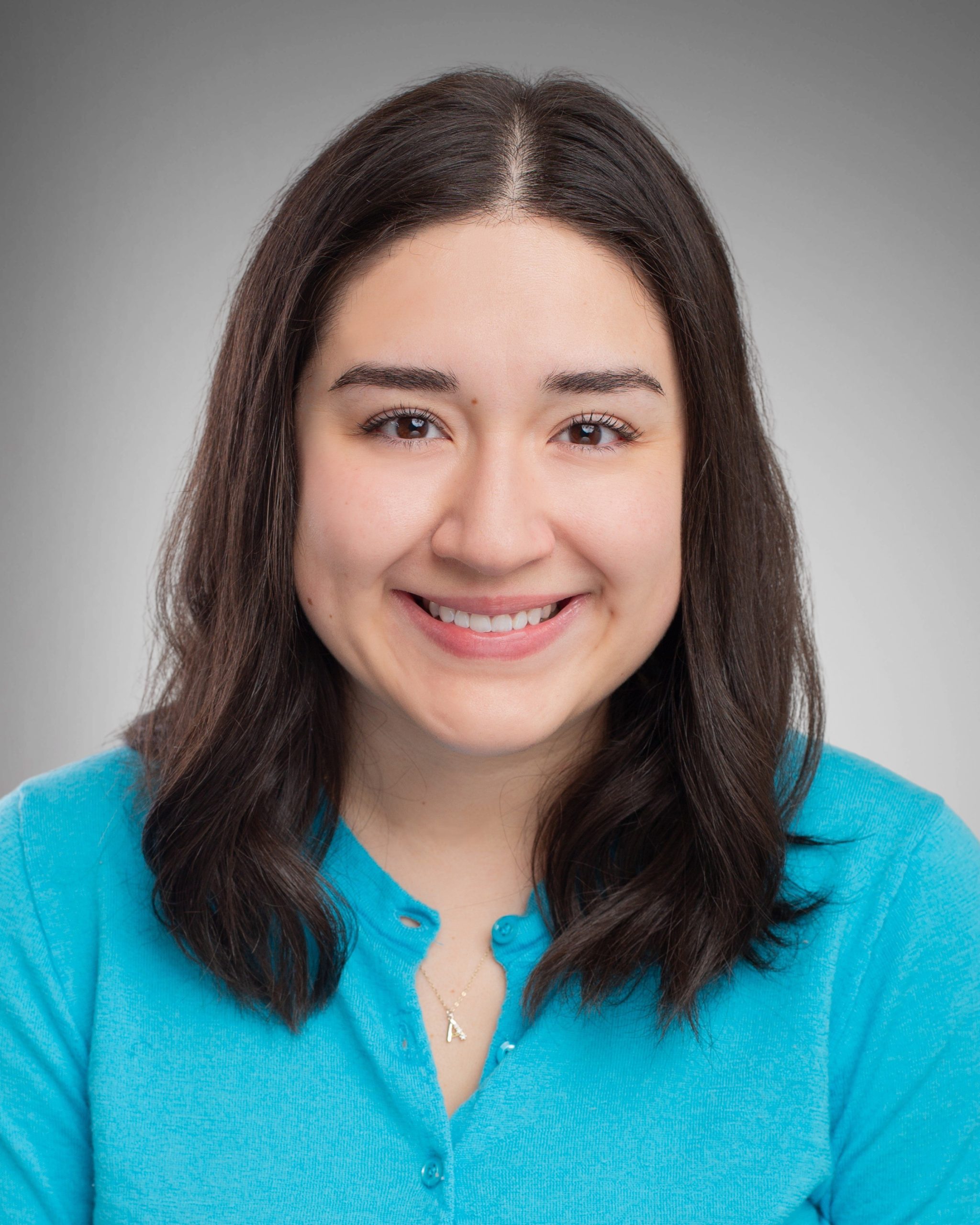 Woman with shoulder length dark hair smiling at camera, wearing teal button-up blouse.