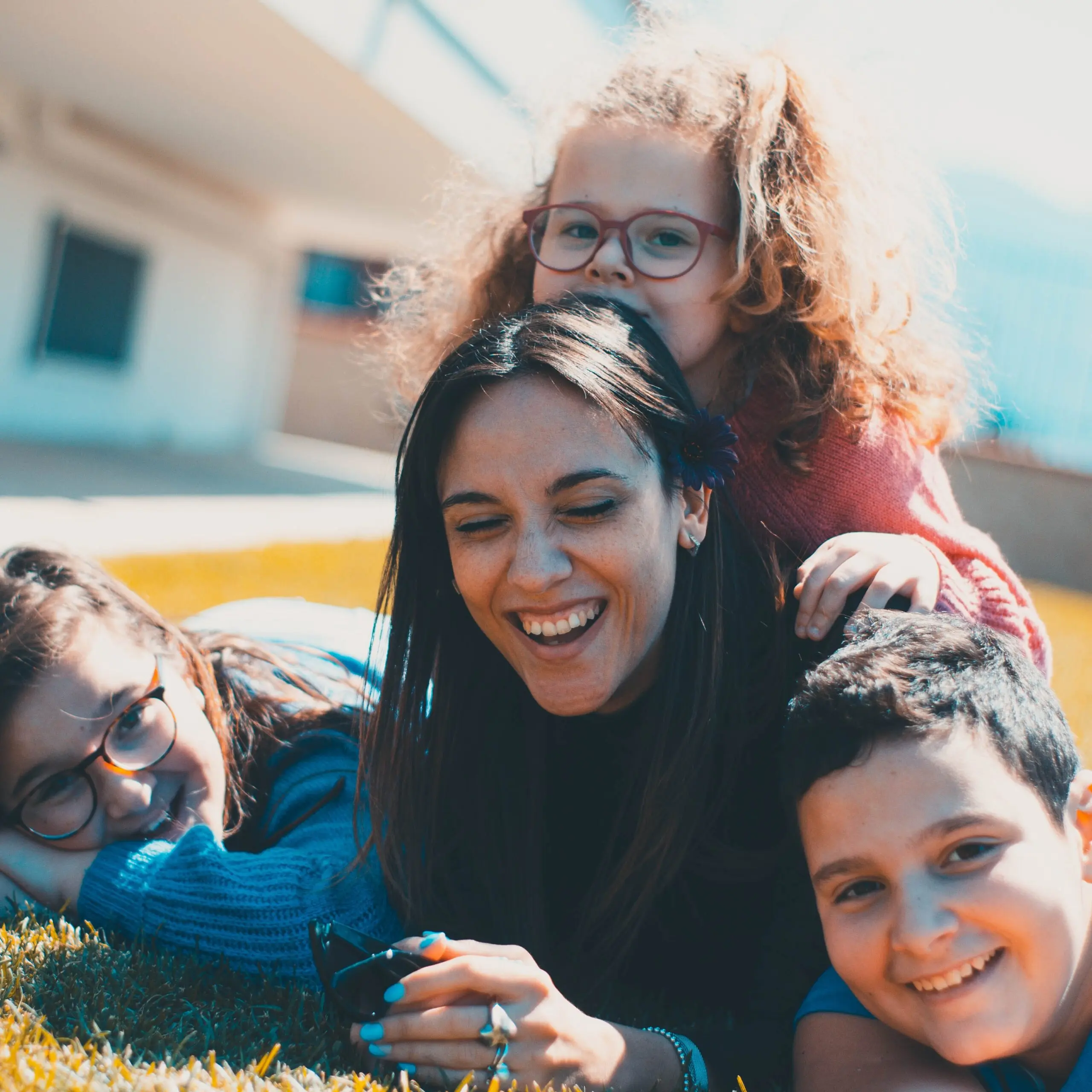 Teen girl lying on the ground and smiling. There are three younger kids with her. They are also smiling.